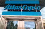 Blue Atlas Copco sign mounted above a modern glass building entrance.