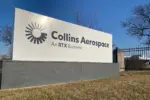 Collins Aerospace sign with logo and "An RTX Business" on a white panel with a gray base, under a blue sky.