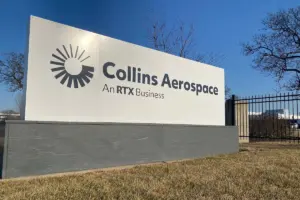 Collins Aerospace sign with logo and "An RTX Business" on a white panel with a gray base, under a blue sky.