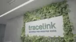 TraceLink logo and slogan Network for Greater Good on a white sign framed by a lush green living wall.