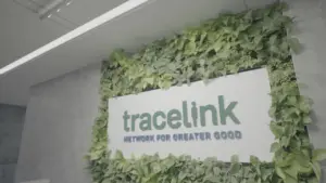 TraceLink logo and slogan Network for Greater Good on a white sign framed by a lush green living wall.