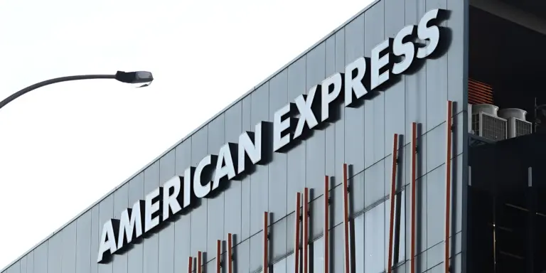 AMERICAN EXPRESS sign in white letters on a modern gray building, with a street light.