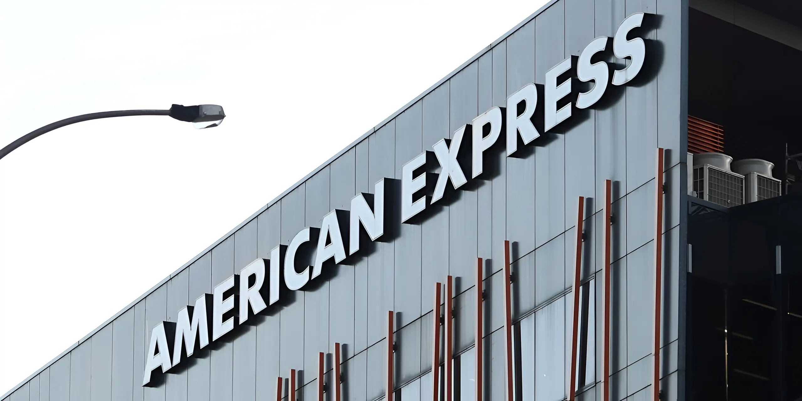 AMERICAN EXPRESS sign in white letters on a modern gray building, with a street light.
